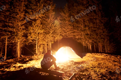 Preview: Male tourist have a rest in his camp near the forest at night