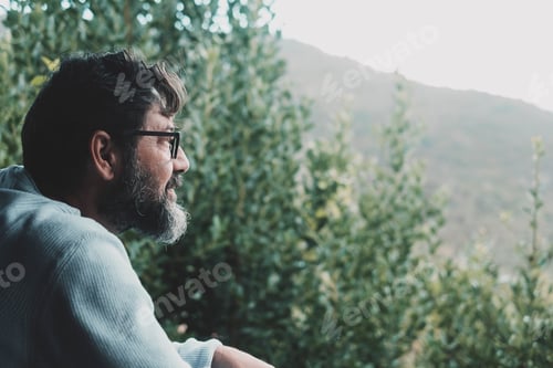 Preview: Side portrait view of mature man with beard and glasses looking the nature woods in background.