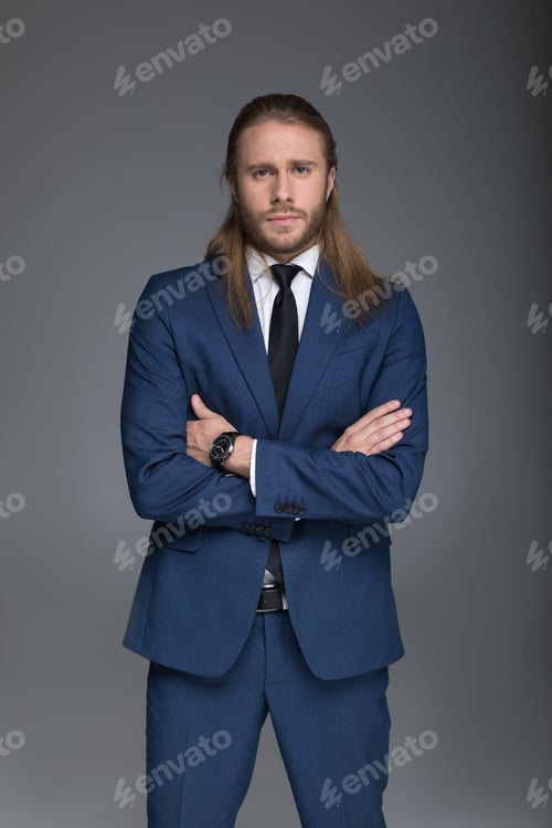 Preview: young confident caucasian businessman in suit standing with arms crossed