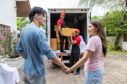 Preview: Young couple checks with two movers unloading boxes and furniture from a pickup truck
