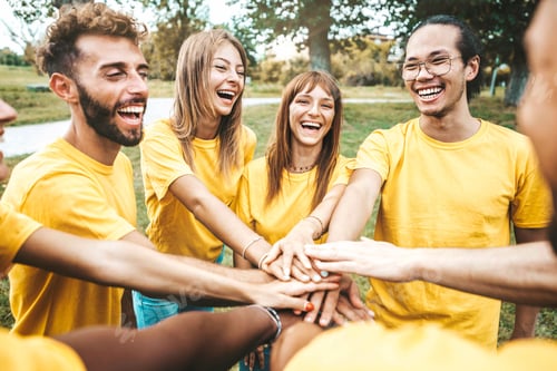 Preview: Multi ethnic young people team stacking hands together outside