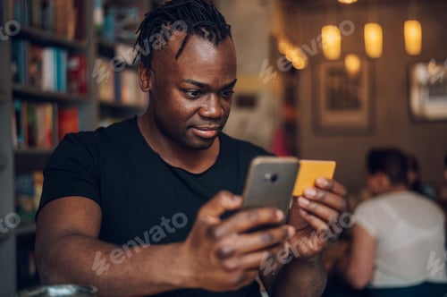 Preview: African american man using smartphone and credit card in a cafe