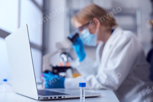 Preview: Female Lab Worker Wearing Lab Coat Working On Covid-19 Vaccine With Laptop And Microscope