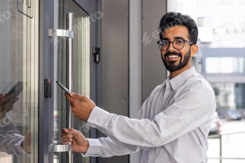 Preview: Confident young businessman with glasses smiling while entering modern office building using