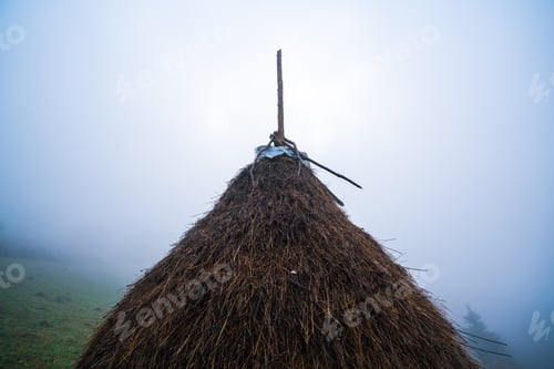 Preview: A large haystack stands on a green field among the dense gray fog