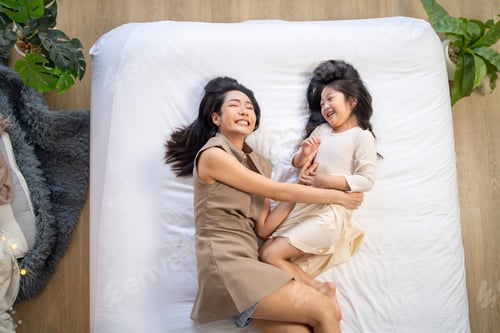 Preview: mother and daughter laughing together while lying on a bed