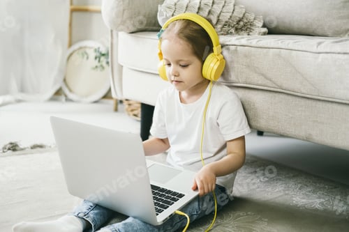 Preview: Little girl 4 years old in yellow headphones in front of a laptop.