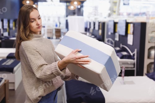 Preview: Young woman chooses mattress and bed in furniture showroom store. Sample of mattress in hands, beds