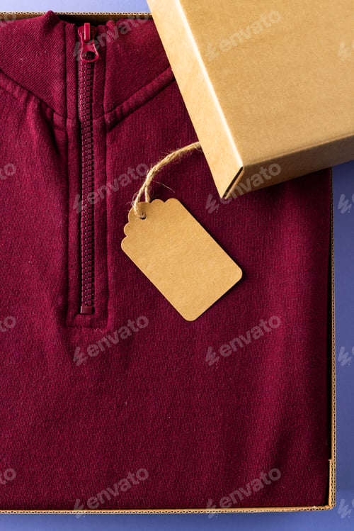 Preview: Close up of red sweatshirt with tag in packaging and copy space on blue background