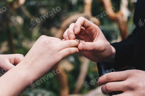 Preview: cropped shot of man putting wedding ring on finger of young bride