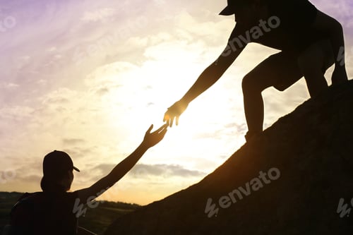 Preview: Silhouettes of man and woman helping each other to climb on hill against sunset