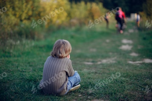 Preview: Sad boy child sits on a path in the park in the forest, a lonely child. Concept Children's emotions
