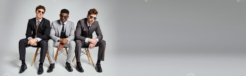 Preview: appealing diverse men with sunglasses in business attires sitting on chairs on gray backdrop, banner