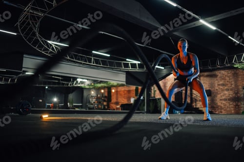 Preview: Determined sportswoman doing exercise with battle ropes during cross training workout