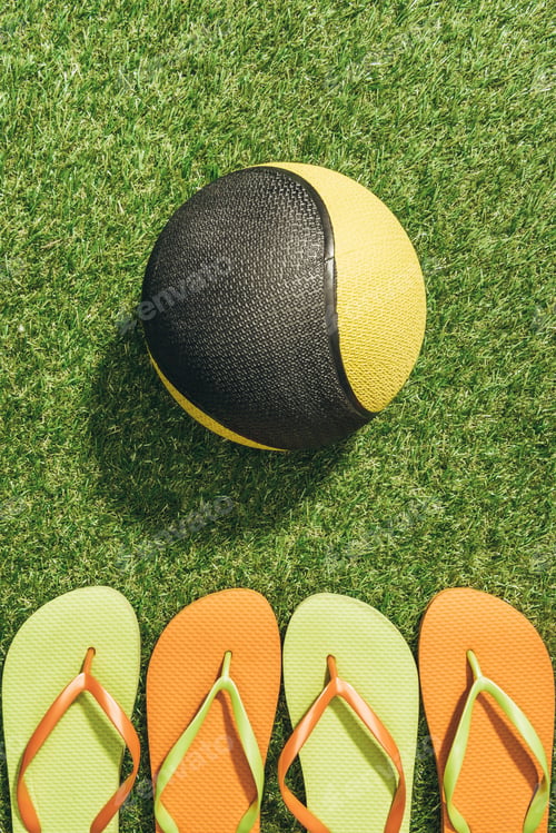 Preview: Top view of medicine ball and colorful flip flops on green grass