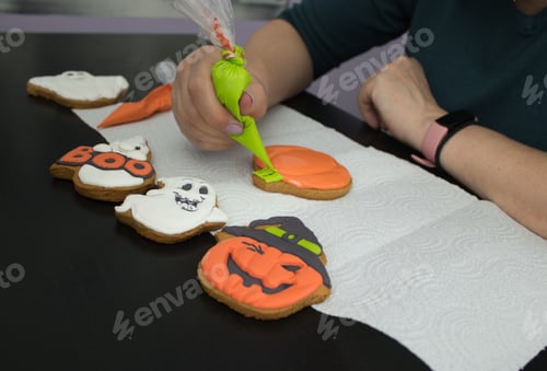 Preview: Women`s hands color a gingerbread in the shape of a pumpkin as a sweet Halloween gift for children