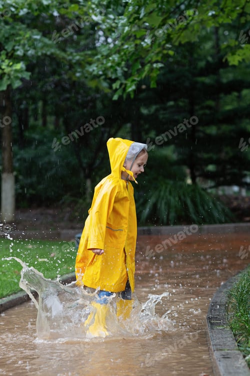 Preview: Caucasian Kid having fun outdoor. Girl wearing yellow raincoat and jumping on puddles at summer day