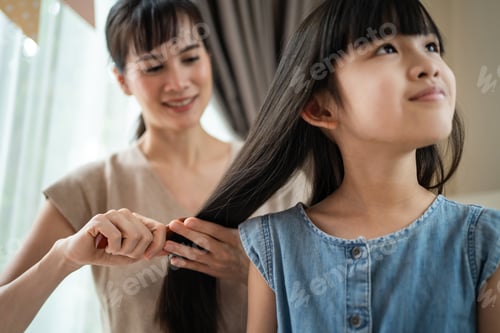 Preview: Woman brushing girl's long hair indoors at home