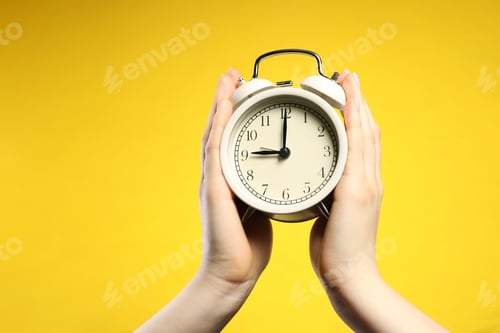Preview: Woman with white alarm clock on yellow background, closeup. Space for text