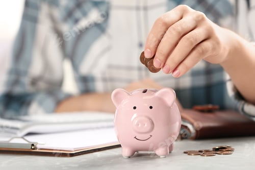 Preview: Woman putting money into piggy bank at table, closeup