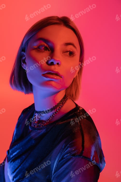 Preview: portrait of woman in necklaces looking away in neon light on pink and coral background