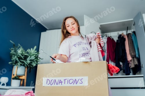 Preview: A cardboard box of selected clothes for donating to a Charity shop standing on the bed. Decluttering