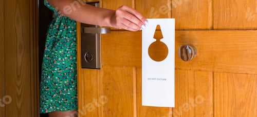 Preview: female hand hangs a sign on the door do not disturb in hotel