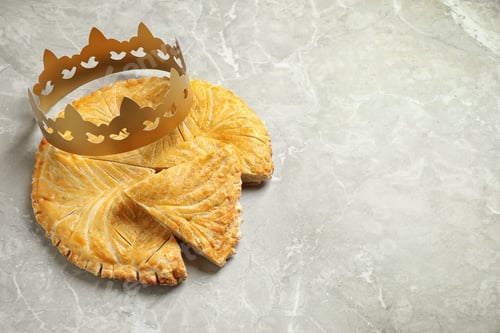 Preview: Traditional galette des Rois with paper crown on grey marble table, above view. Space for text