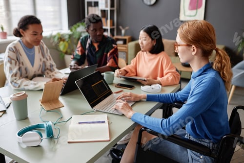 Preview: Young woman in wheelchair using laptop during meeting with diverse team