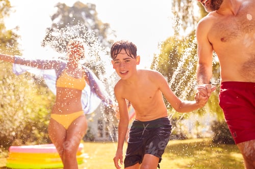 Preview: Family Running Through Water From Garden Sprinkler Having Fun Wearing Swimming Costumes