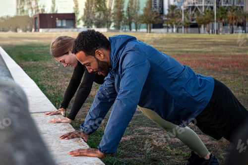 Preview: Happy young multiracial couple doing plank pose outdoors in city park. Couple workout together.