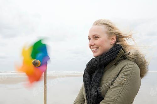 Preview: Smiling woman enjoying a breezy day at the beach with a colorful pinwheel