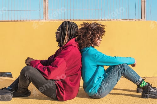 Aperçu: Multiethnic diverse couple wear hoodie relaxing sitting back to back against yellow wall on street