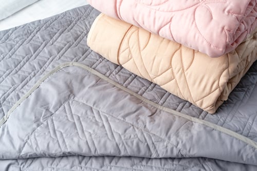 Preview: Stacked Pink And Peach Quilted Blankets On A Gray Bed