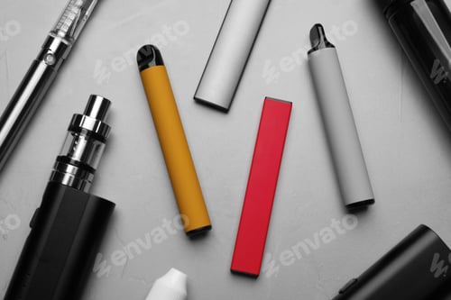 Preview: Different electronic cigarettes on grey table, flat lay. Smoking alternative