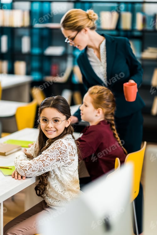 Visualização: adorável estudante sorrindo para a câmera enquanto estuda com colega e professor na biblioteca