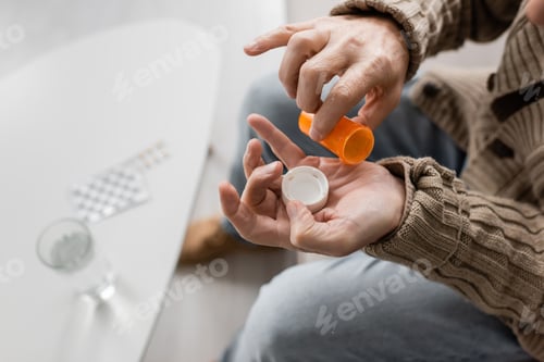 Preview: partial view of man with parkinson disease and tremor in hands holding pills container near blurred