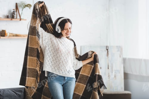 Preview: attractive happy woman dancing with blanket while listening music with headphones