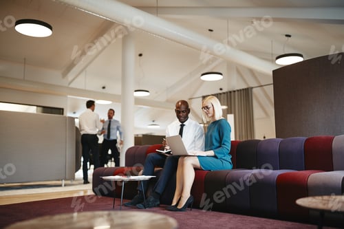 Preview: Two diverse office colleagues working online together on a sofa