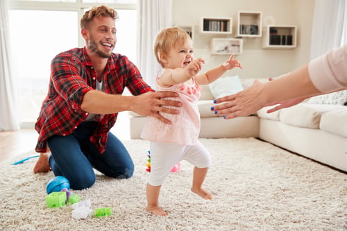 Preview: Toddler girl walking from dad to mumÕs arms in sitting room