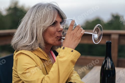 Preview: Mature woman drinking red wine outdoors on terrace during relaxed evening moment