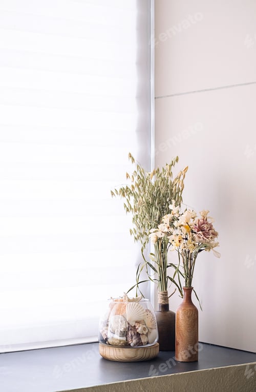 Preview: Dried floral arrangement and seashells in rustic vases on windowsill by window.