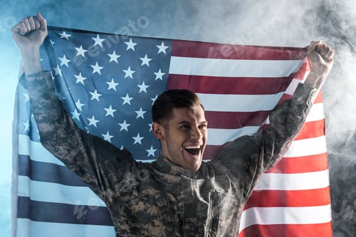 Preview: happy soldier gesturing while holding american flag on black with smoke