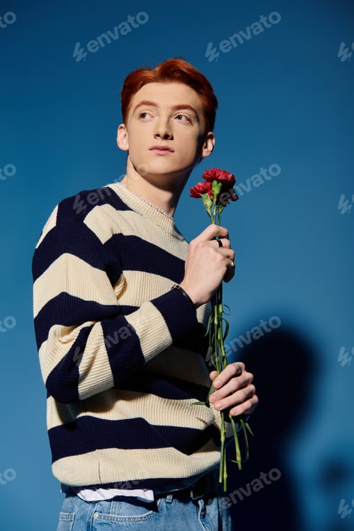 Preview: Emotional young man with a flower poses against a vibrant blue background