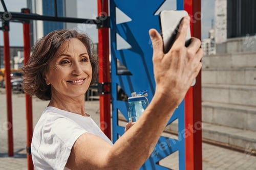 Preview: Jolly mature female taking selfie on sports ground
