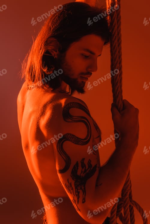 Preview: Sexy tattooed model holding rope isolated on red