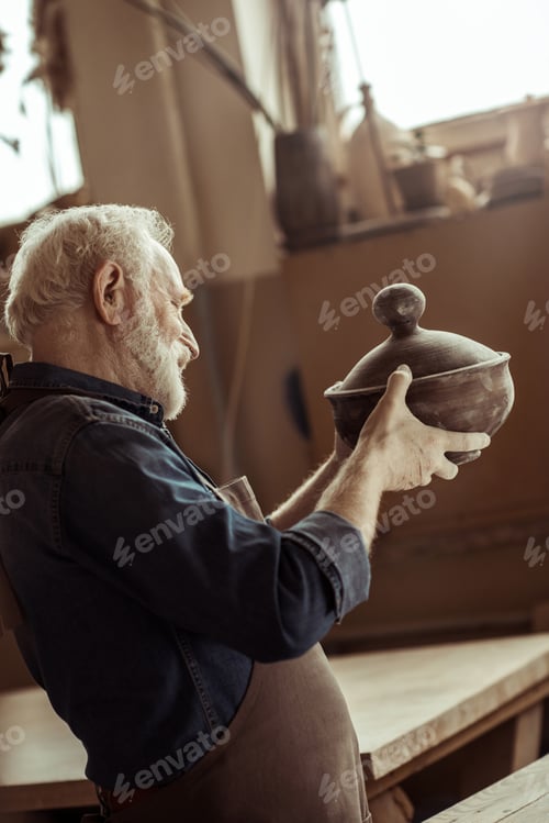 Visualização: Ceramista sênior em avental examinando tigela de cerâmica na oficina