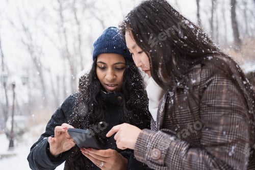 Preview: two asian women looking at phone screen outdoors in winter park for navigation