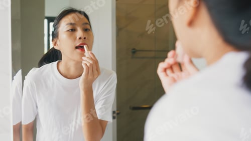 Preview: Woman make up looking at her reflection in mirror apply lip balm on her lips in bathroom.