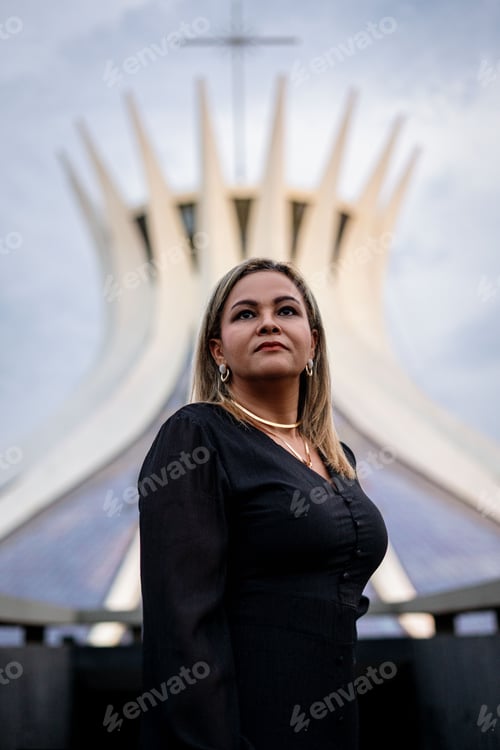 Preview: Of a woman in her 30s standing in front of the Cathedral of Brasilia, Brazil, under a cloudy sky.
